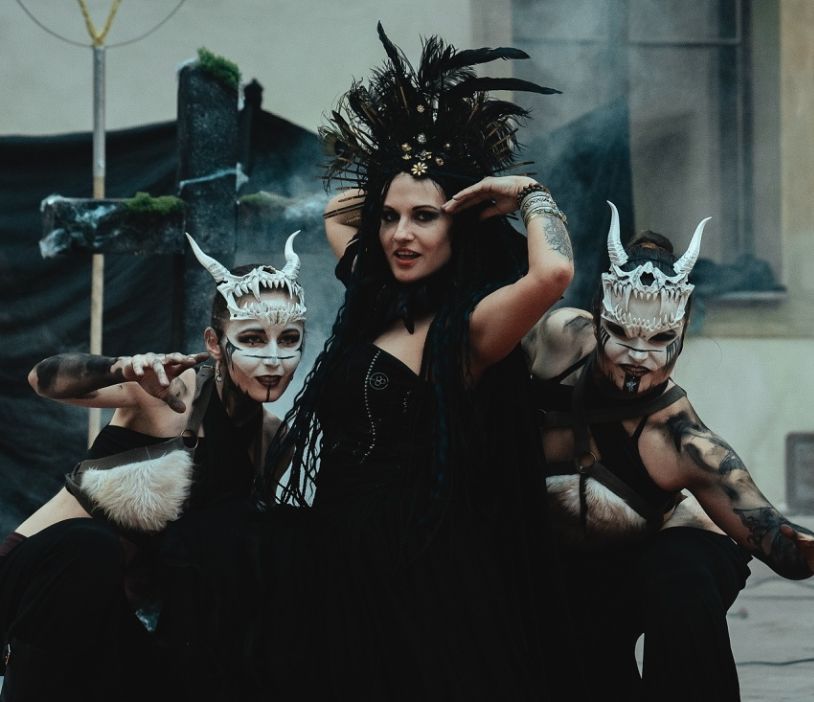 Žena v černém korzetu a péřové pokrývce hlavy pózuje mezi dvěma postavami s rohatými maskami na plese Mystic Star